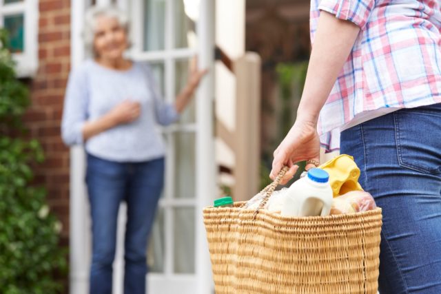 Hauswirtschaftliche Hilfe bringt Einkauf zur Haustür_Seniorin öffnet lächelnd die Tür