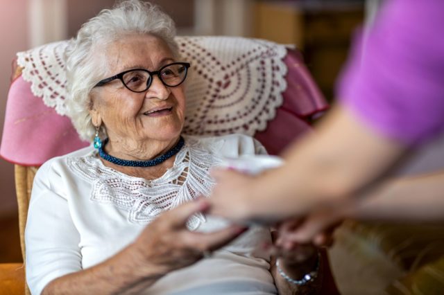 Lachende Seniorin greift nach Hand der Pflegerin