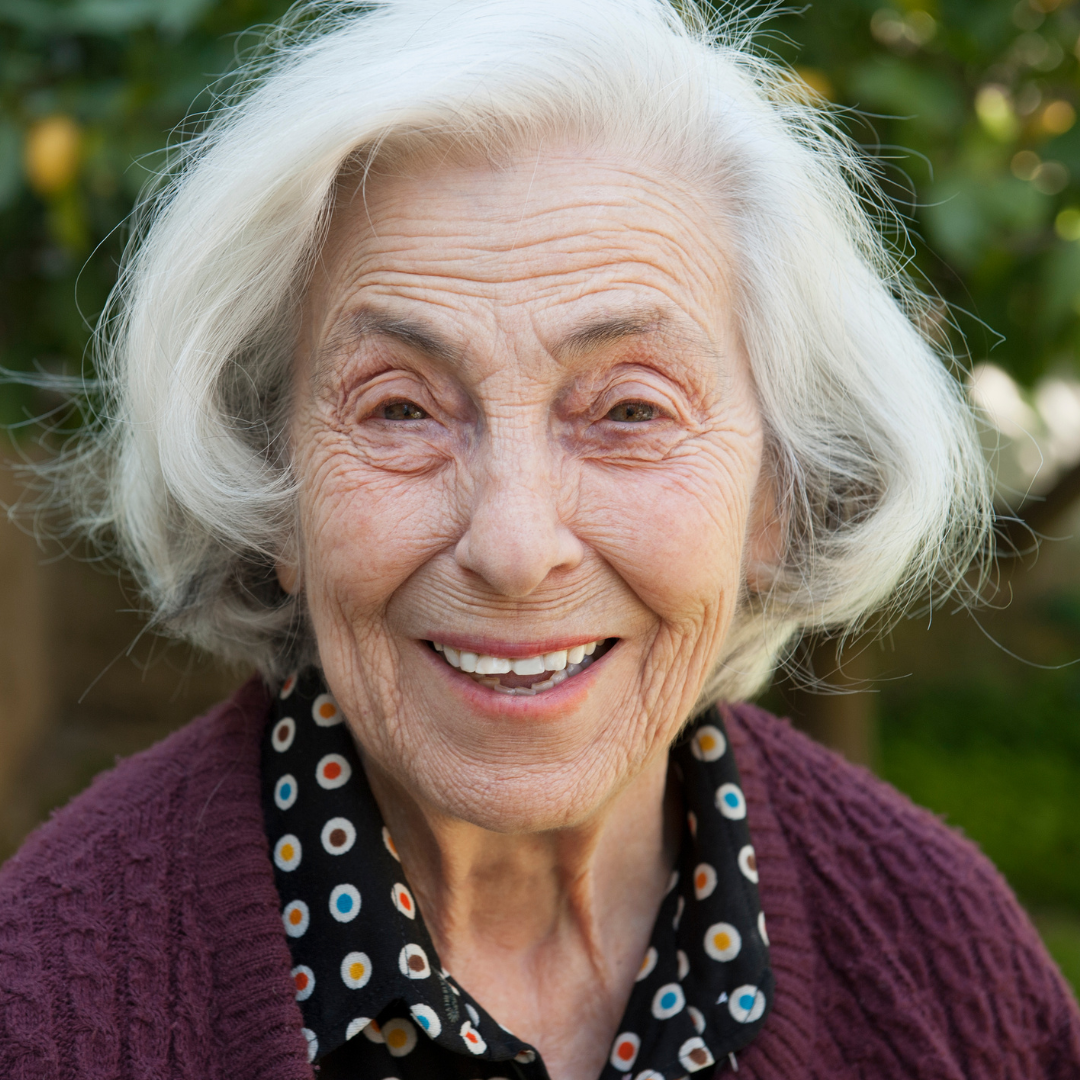 Kundin, namens Anna, ungefähr 80 Jahre alt, kinnlange weiße Haare, lachend im Garten. Hat eine ausgezeichnete Bewertung für den ambulanten Pflegedienst abgegeben hat.