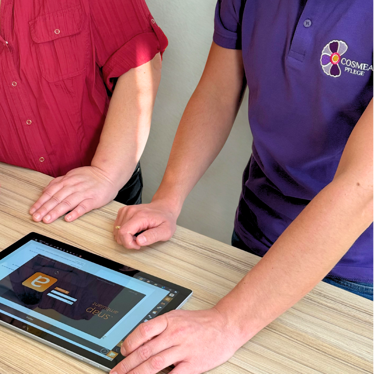 Pflegefachkraft und Betriebsleiter sehen aus ein Tablet und öffenn SNAP ein Programm zur Tourenplanung. Eine Pflegefachkraft trägt ein lila Cosmea Pflege Polo Shirt.
