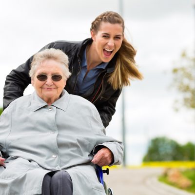 Fröhliche Pflegefachkraft mit Senioren im Rollstuhl